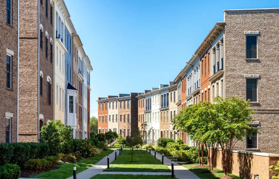 Row of modern townhouses with front gardens under a clear blue sky.