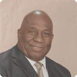 Portrait of a smiling man in a suit and tie against a neutral background.